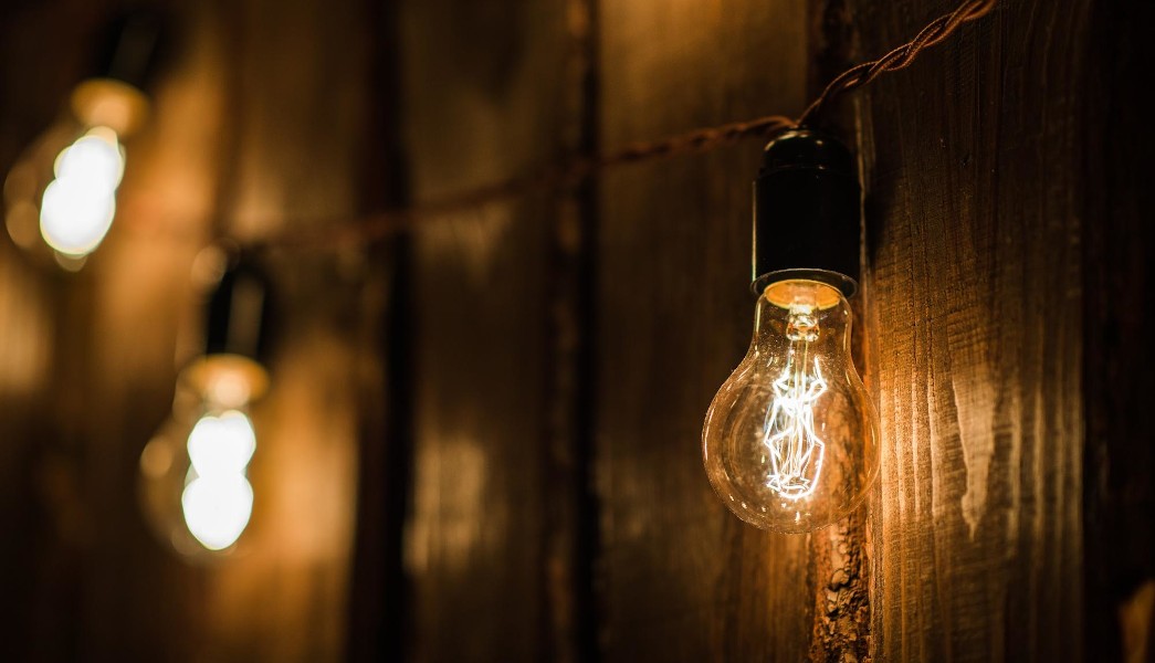 Lâmpada retrô com plugue e cabo pendurado na parede de madeira.