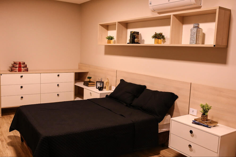 foto de um quarto planejado cômoda baixa, cama e prateleira aérea acima da cama.